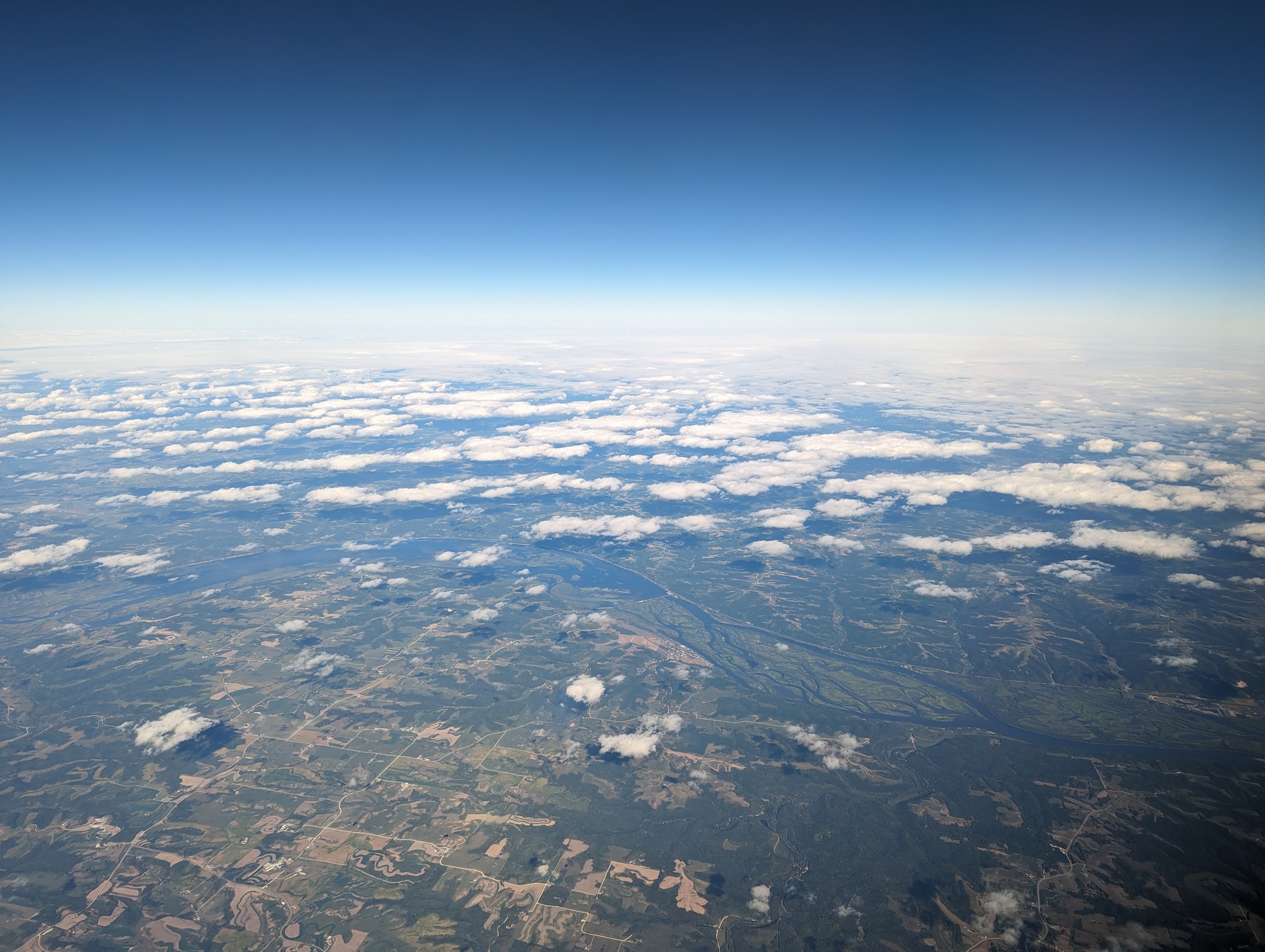 A photograph of clouds above earth taken from an airplane. The clouds form a striped pattern across the sky.