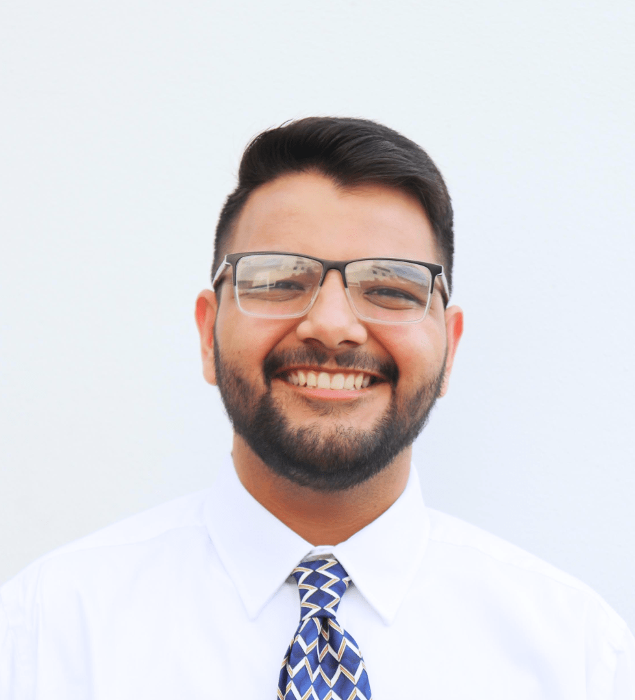 Portrait photo of a smiling bearded man with dark hair and glasses