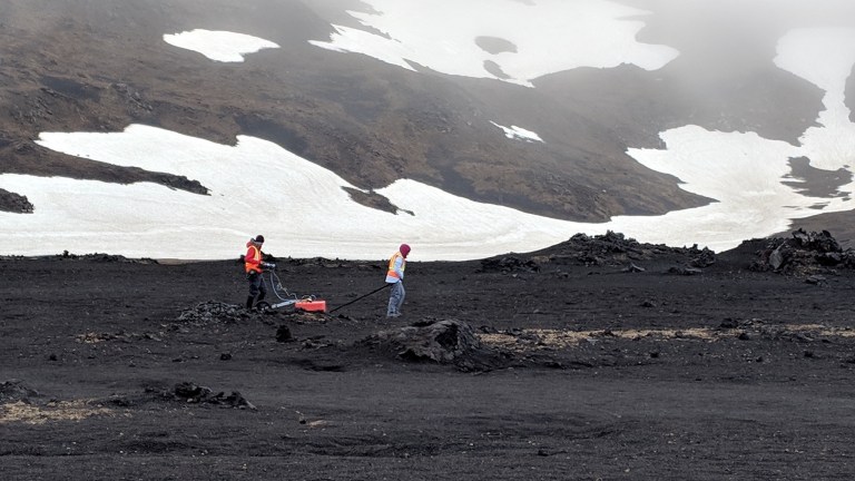 Scientists maneuver gear on the dark ground near ice.