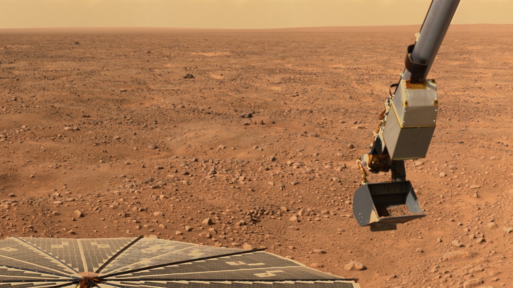 A spacecraft's scoop hangs above the red soil of Mars. The spacecraft's solar arrays can be seen to the left of the scoop.