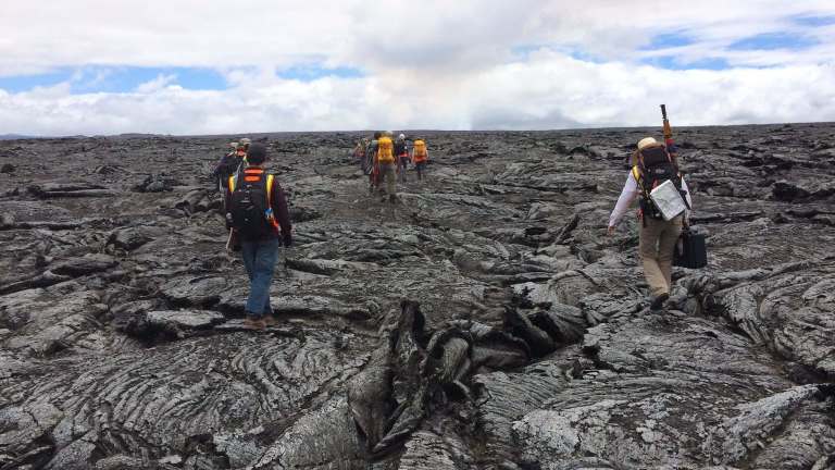 Scientists carry gear as the navigate the slopes of a volcano.