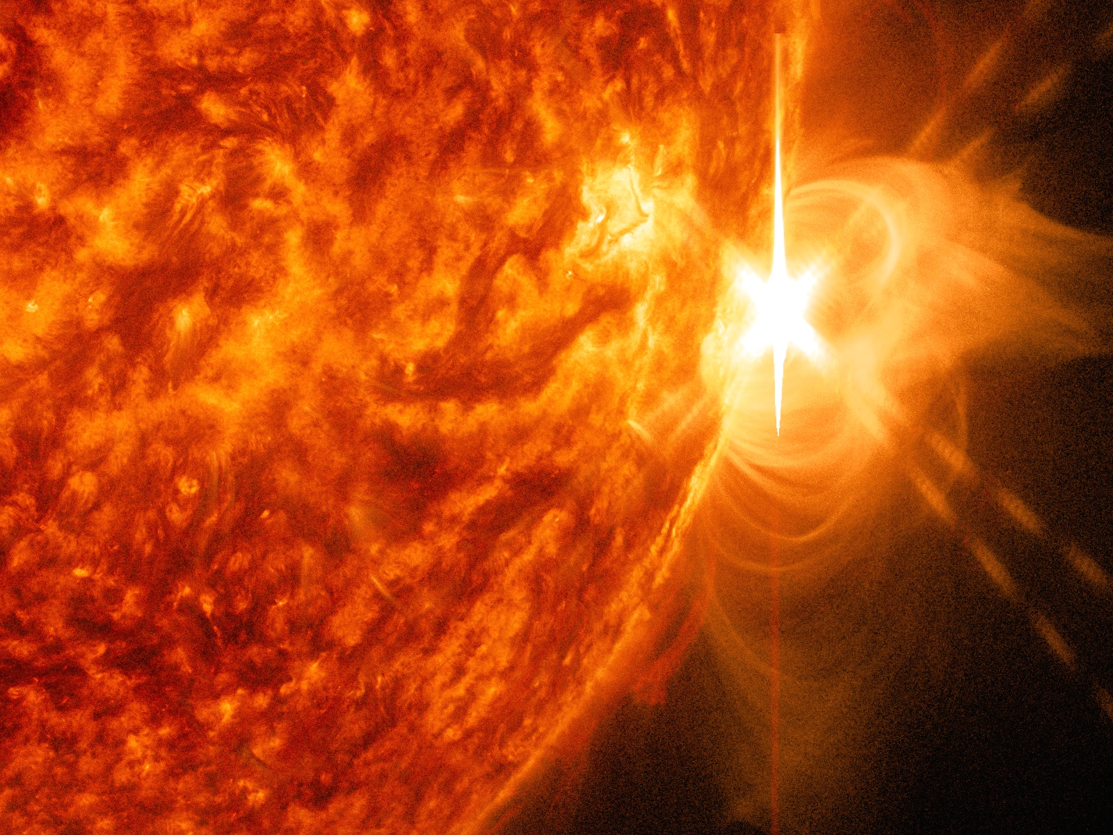 A close-up image of the Sun with a large bright spot and filaments of solar material spewing out from it.