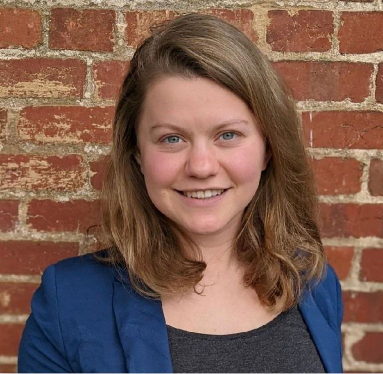 Headshot of Mary Guenther in a blue blazer in front of a red brick wall.