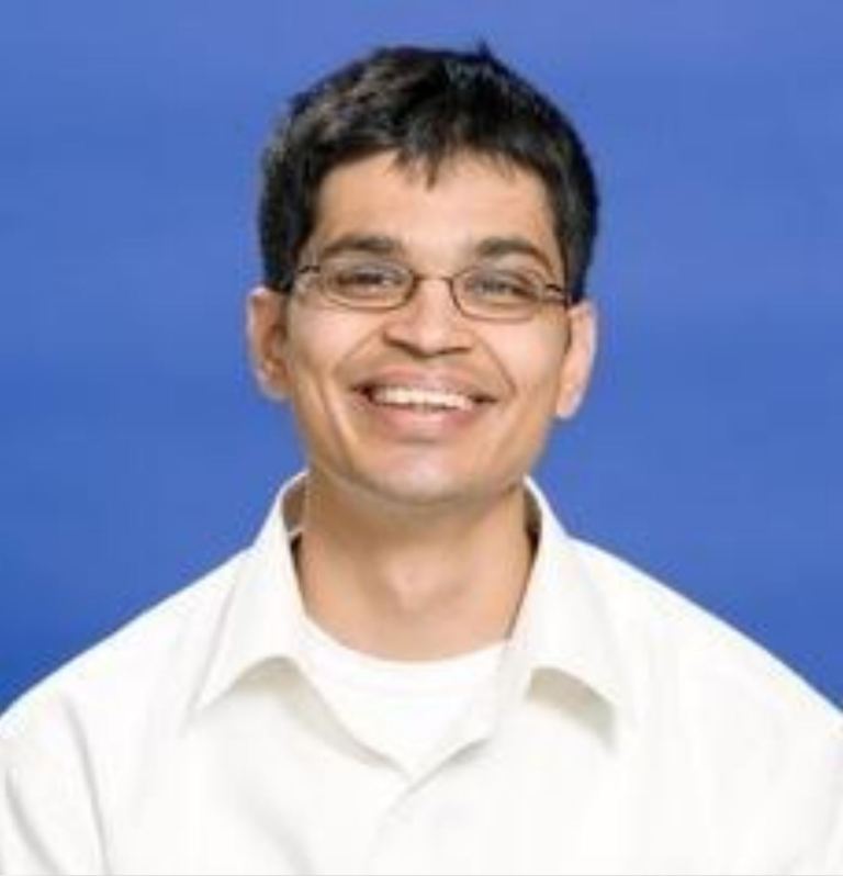 Portrait of Ali Rangwala in glasses and an off-white button-up shirt.