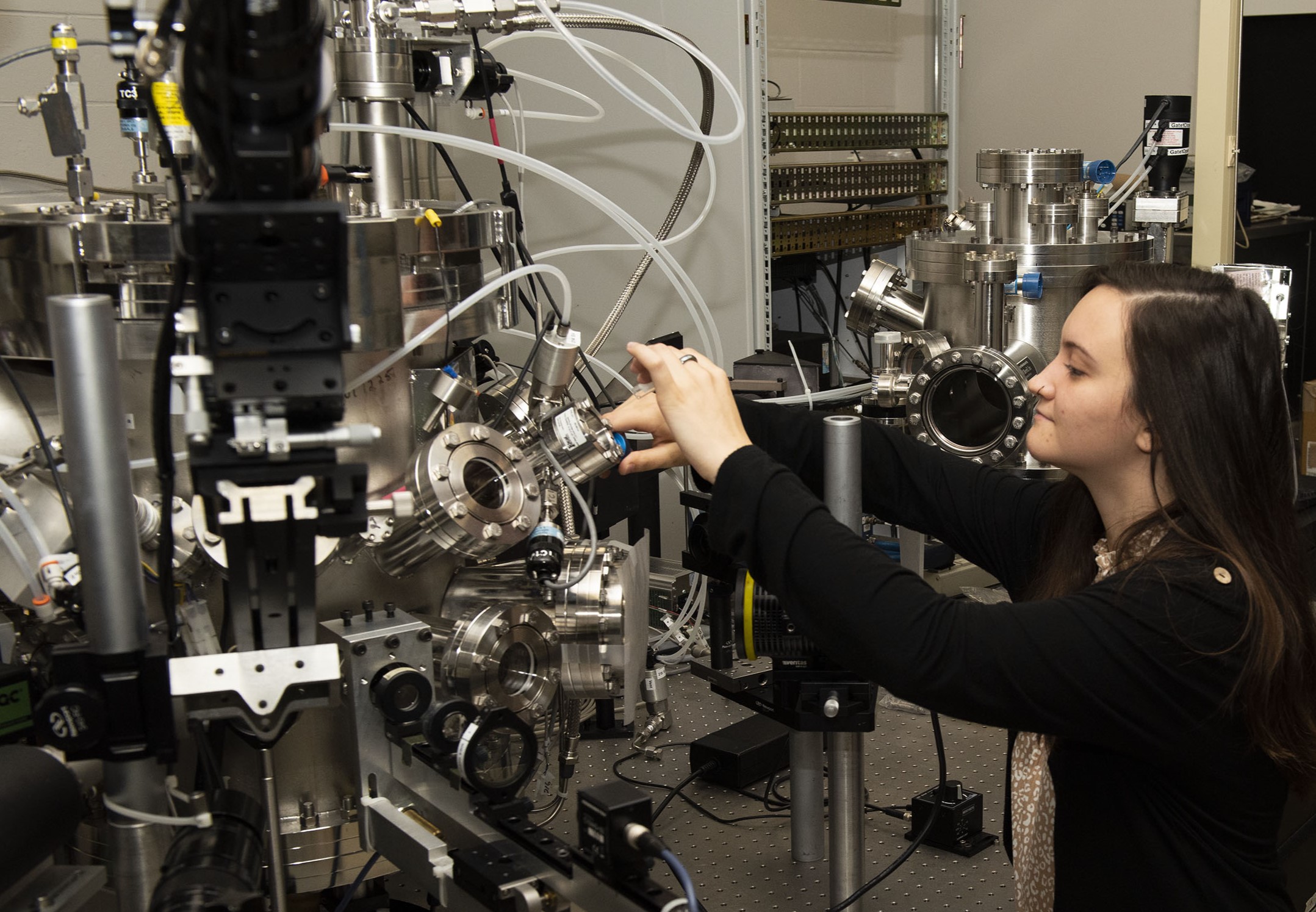 A person stands in front of a scientific machine not looking at the camera.