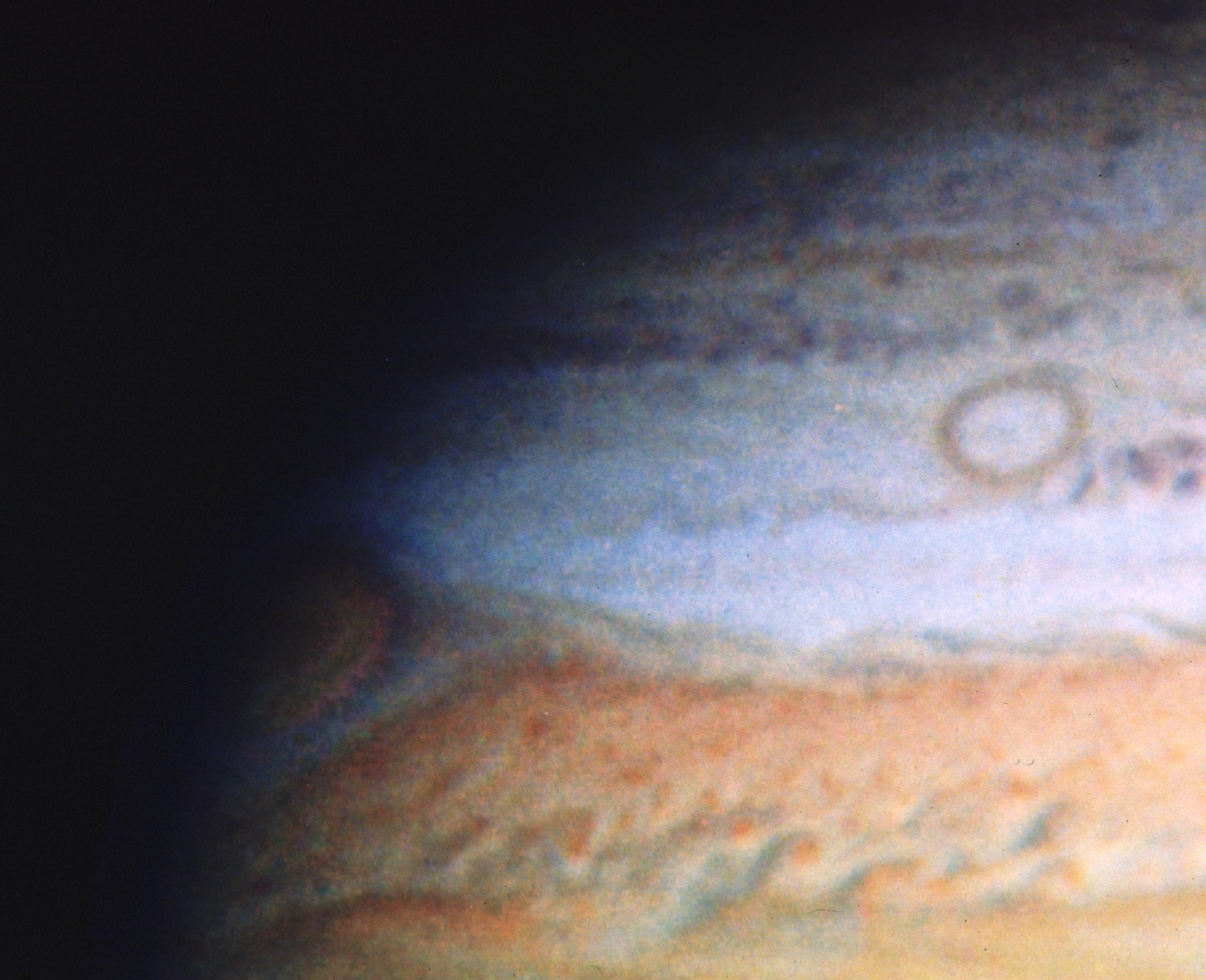 Only a quarter of the planet Jupiter is visible extending from the lower-right corner across the image. Colors of orange, rusty-red, and white bands.