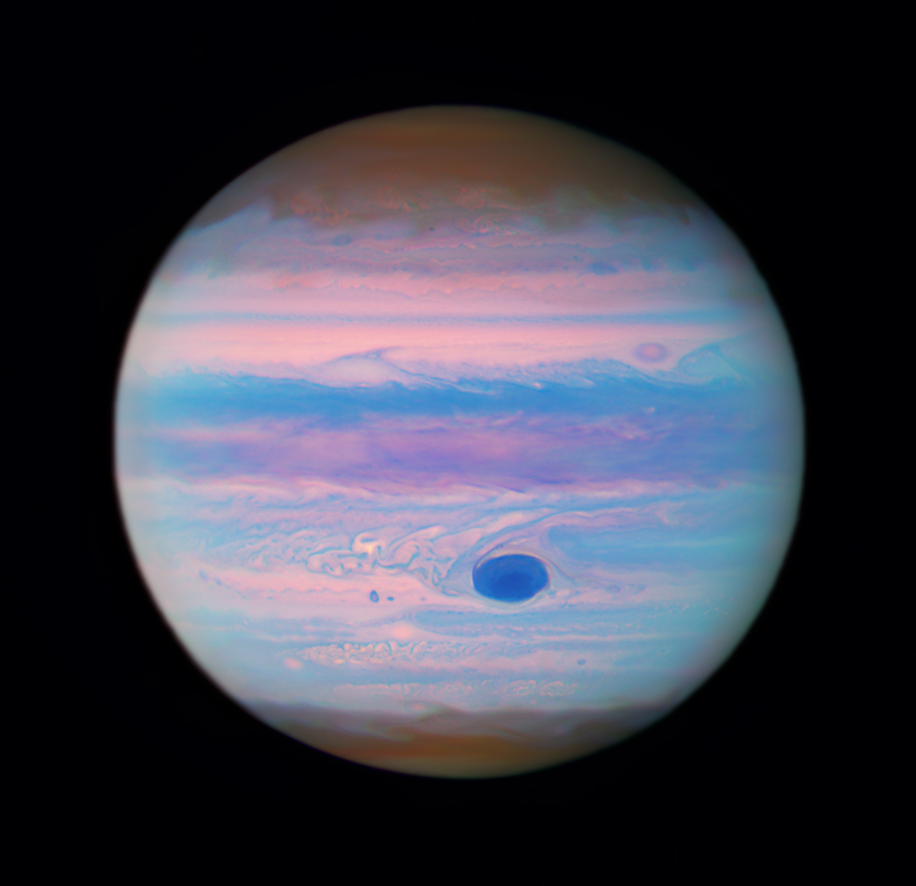The planet Jupiter with its familiar cloud bands seen in shades of pink, rusty red, blue, and purple. The Great Red Spot is a deep navy blue, surrounded by bands and swirls of pink, and light blue.