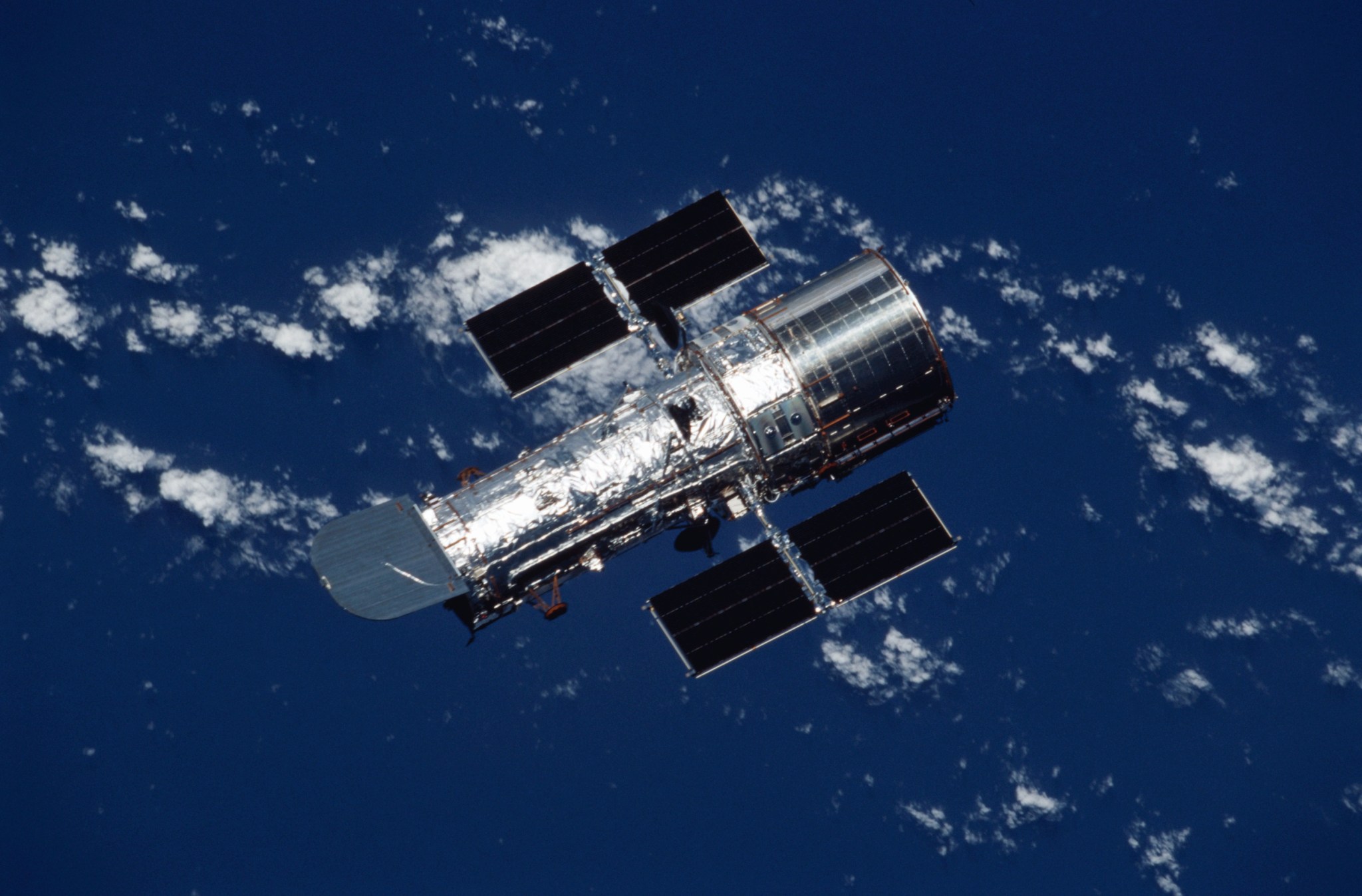 Hubble orbits above Earth and its blue oceans and white clouds as a backdrop.