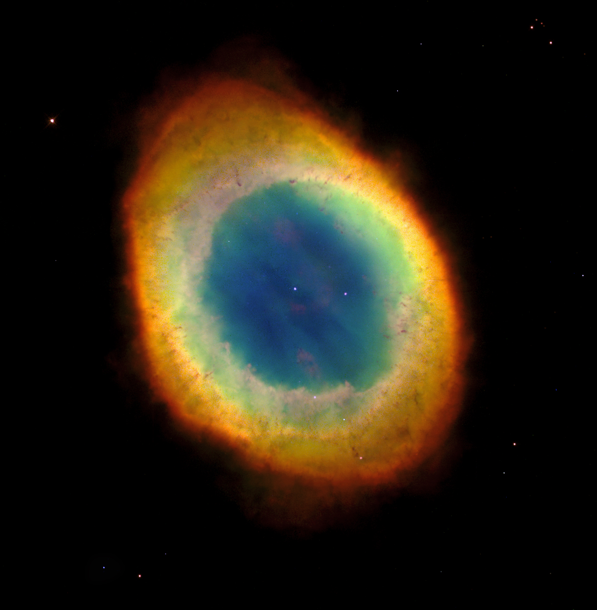 An beautifully colored ring of gas and dust. The ring is slightly elongated/egg-shaped. The center of the ring is blue with two stars visible inside of it (one directly in the center). Beyond the blue center are rings of color. First is green, then yellow, orange, and red.