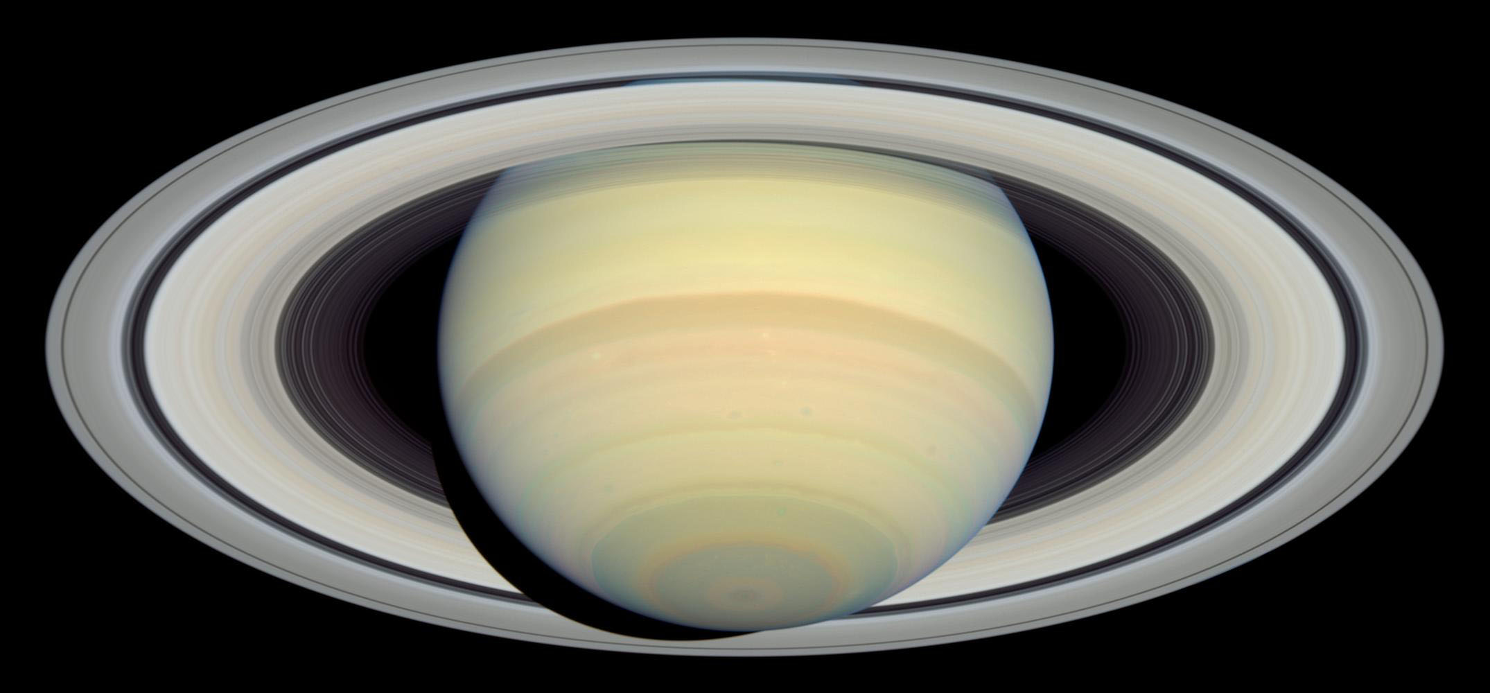 Saturn and its rings. The planet appears as though it is tilted backward, appearing to reveal the underside of its rings. Overall Saturn is yellow with bands of red, yellowish-brown, light orange, pink, and blue.