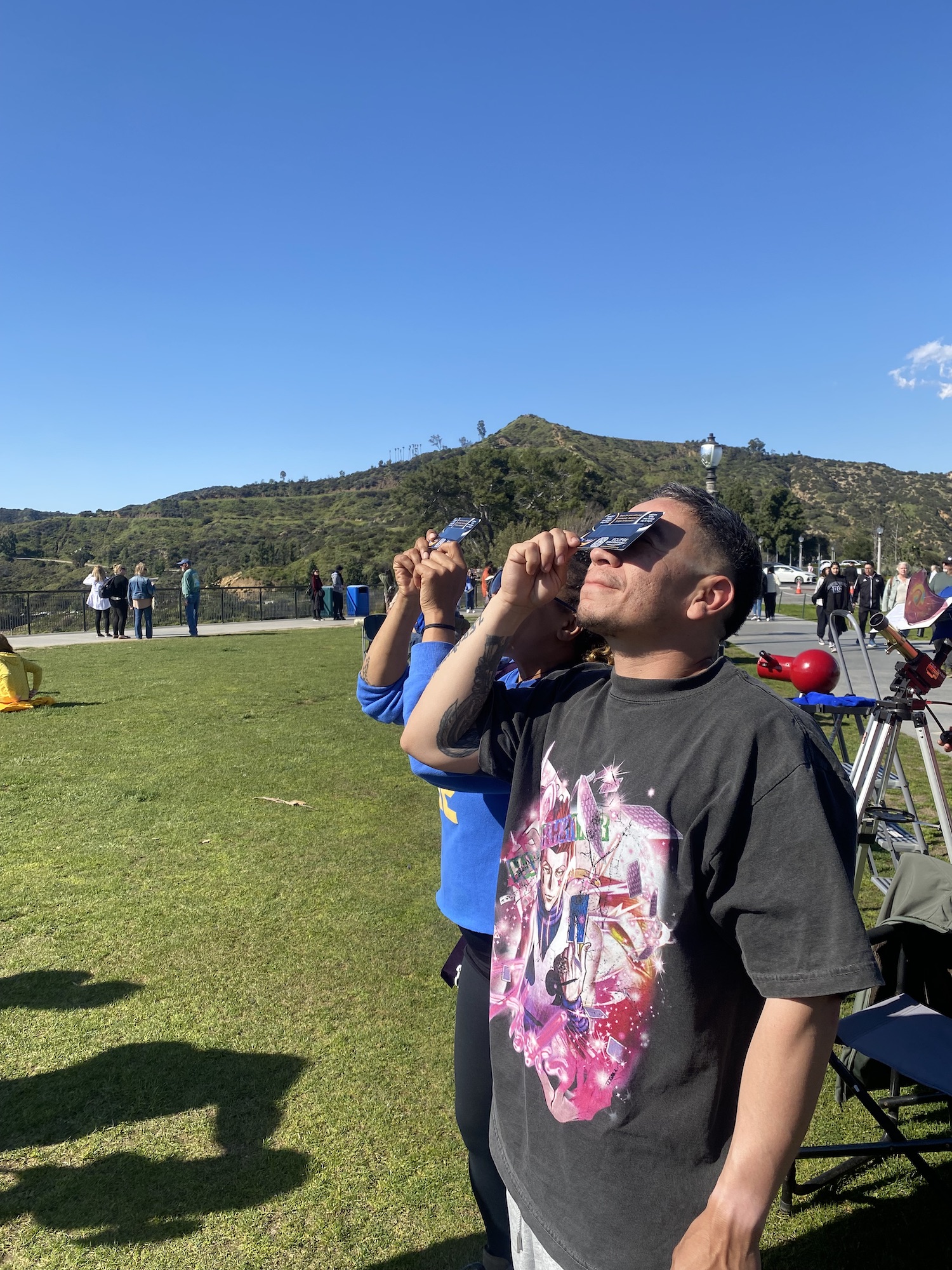 Two people stand looking up at the Sun, while holding solar filters against their eyes.