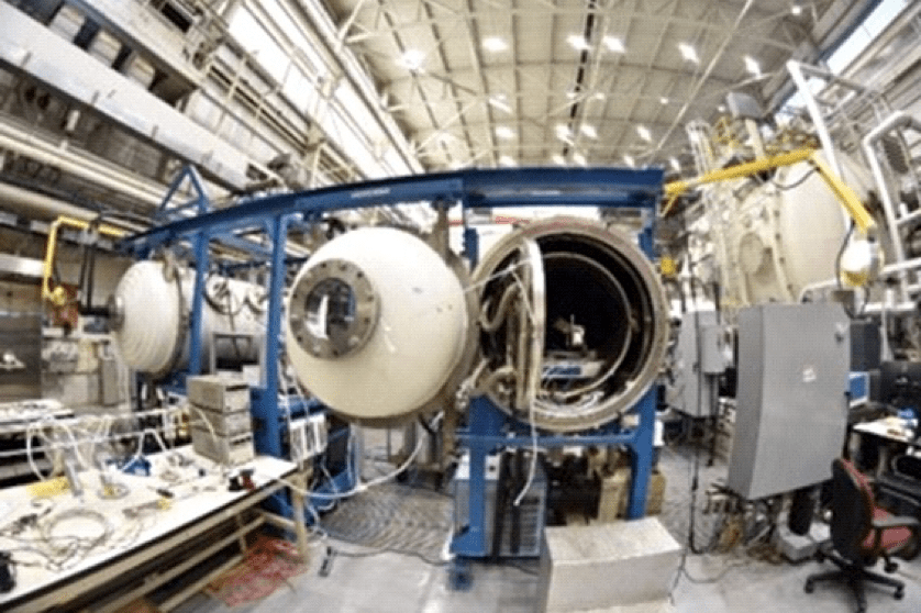 A laboratory containing several large tubes with protruding wires and tubes. The door to the tube in the center is open, showing the equipment inside the tube.