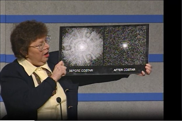 Sen. Barbara Mikulski is on the left side of the image. To her right she holds an image comprised of two Hubble images. The image on the left is of a star before the installation of COSTAR. It is bright-white and extended, filling the frame. To the right is an image of a star after COSTAR was installed. The star is a bright-white disk in the center of the image.