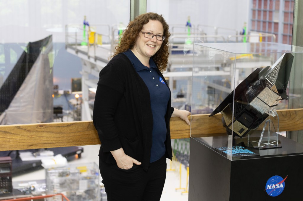 A woman stands beside a telescope model