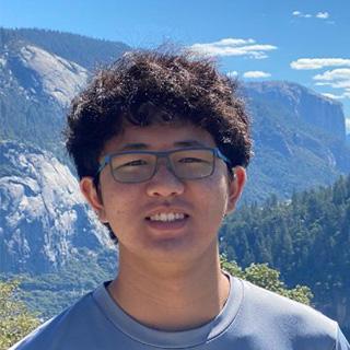 Portrait photo of a young man wearing glasses with a mountainscape in the background