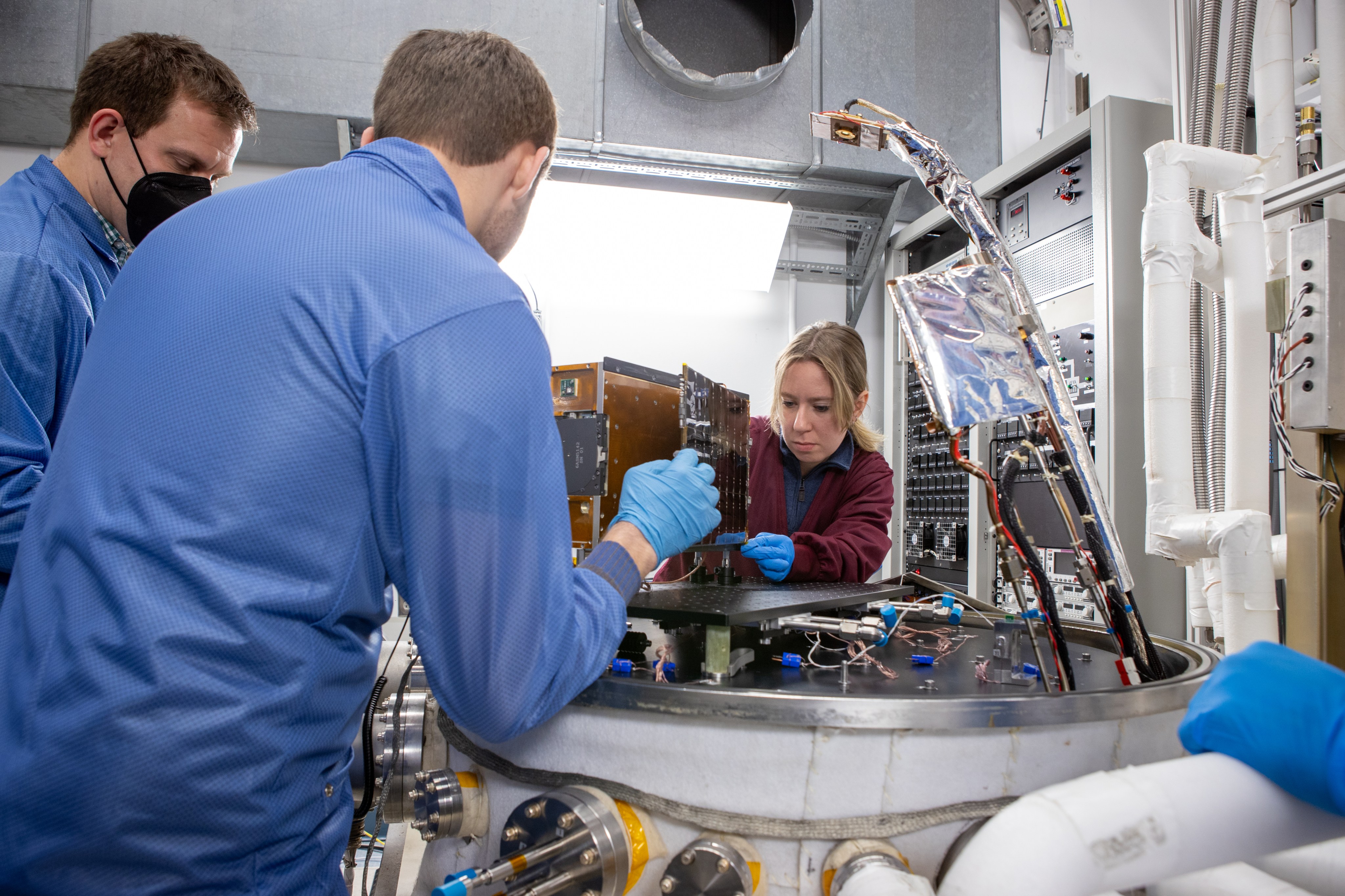 This photograph shows three people working on a spacecraft in a lab.
