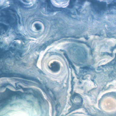 White swirls of cloud play across this mostly blue image. A prominent swirl of white in the middle surrounds a darker blue spot. This is a dark vortex. A second spot of the same dark blue is above and left. The image also contains a red vortex in the lower right corner, and two white vortices. The larger of the white vortices is in the lower left corner, mostly out of the frame, with a pale green tinge. The smaller is in the lower right, adjacent to the trailing clouds of the dark vortex in the middle of the image.