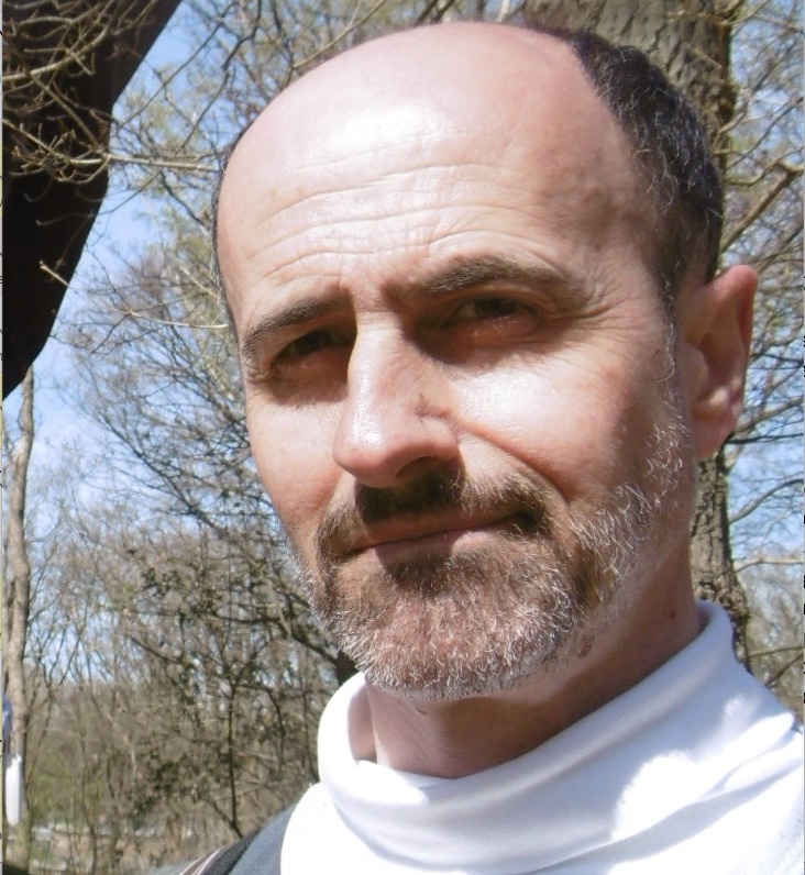 Portrait photo of a balding man with light blue sky and trees in the background.