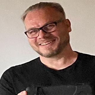 Portrait photo of a smiling young man in a black tshirt and glasses.