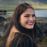 Portrait photo of a young smiling woman with long dark hair, looking over her shoulder.