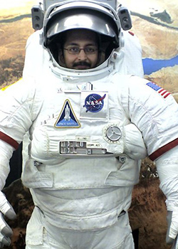 Photo of a man wearing glasses wearing an astronaut suit.