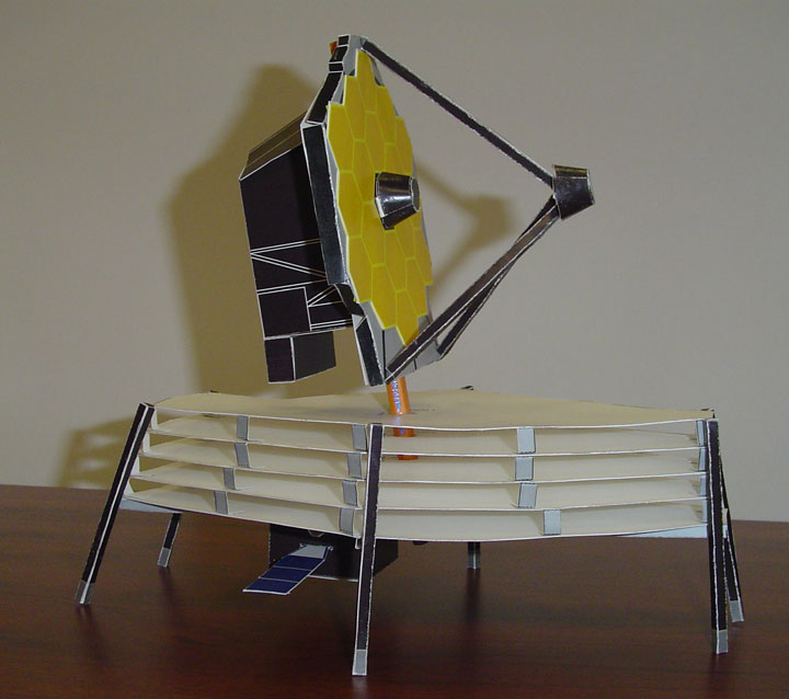 A view of a paper model of the James Webb Space Telescope standing on a desk table.