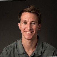 Portrait photo of a smiling man with dark hair against a dark background.