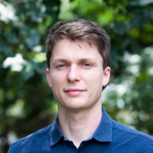 Portrait photo of a man standing outside with green trees in the background.