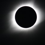 The wispy solar corona shines brightly behind the dark disk of the Moon during a total solar eclipse