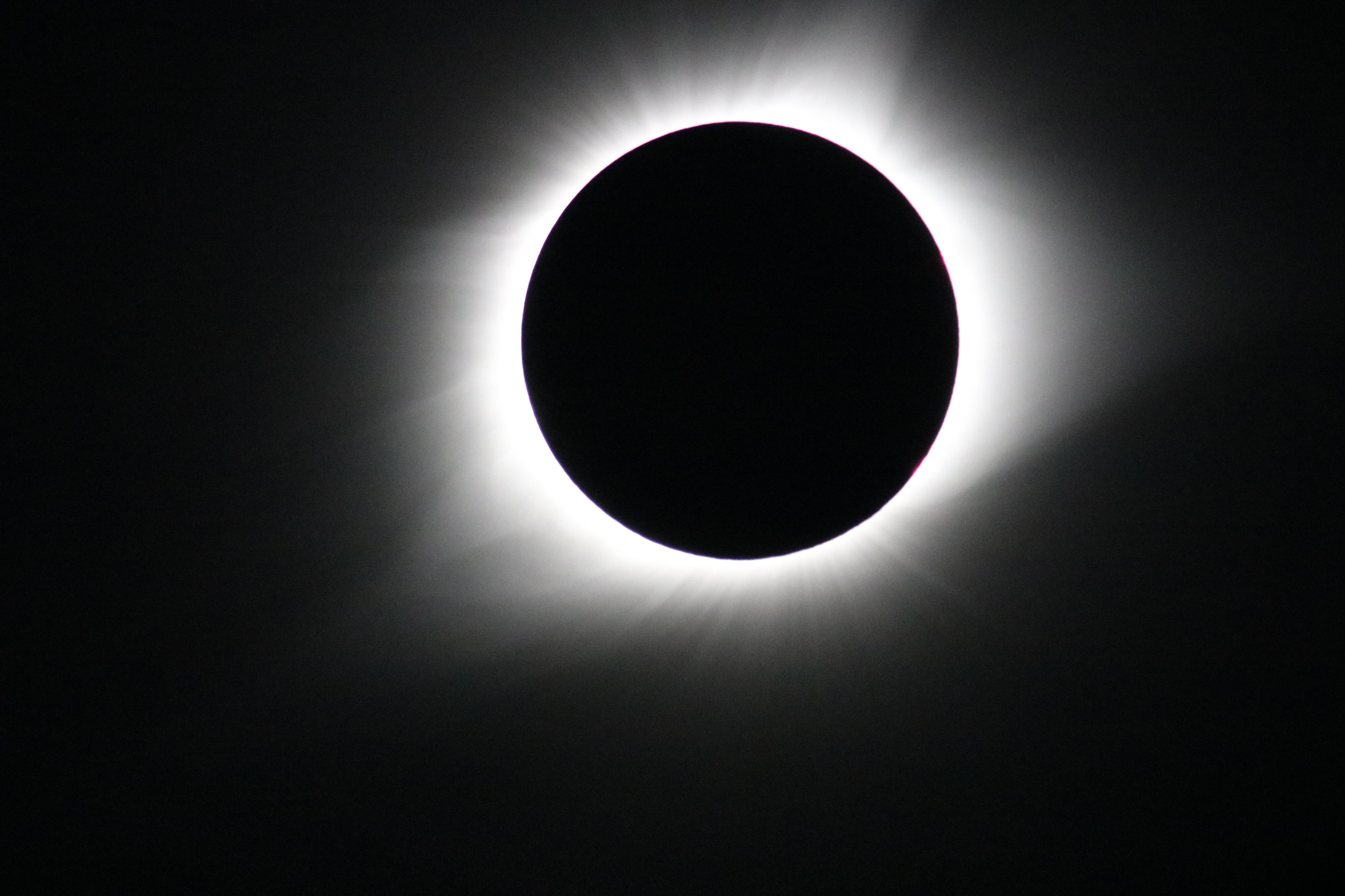 The wispy solar corona shines brightly behind the dark disk of the Moon during a total solar eclipse