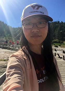 Selfie photo of a woman wearing glasses, a ball cap and standing outside with the sun behind her.