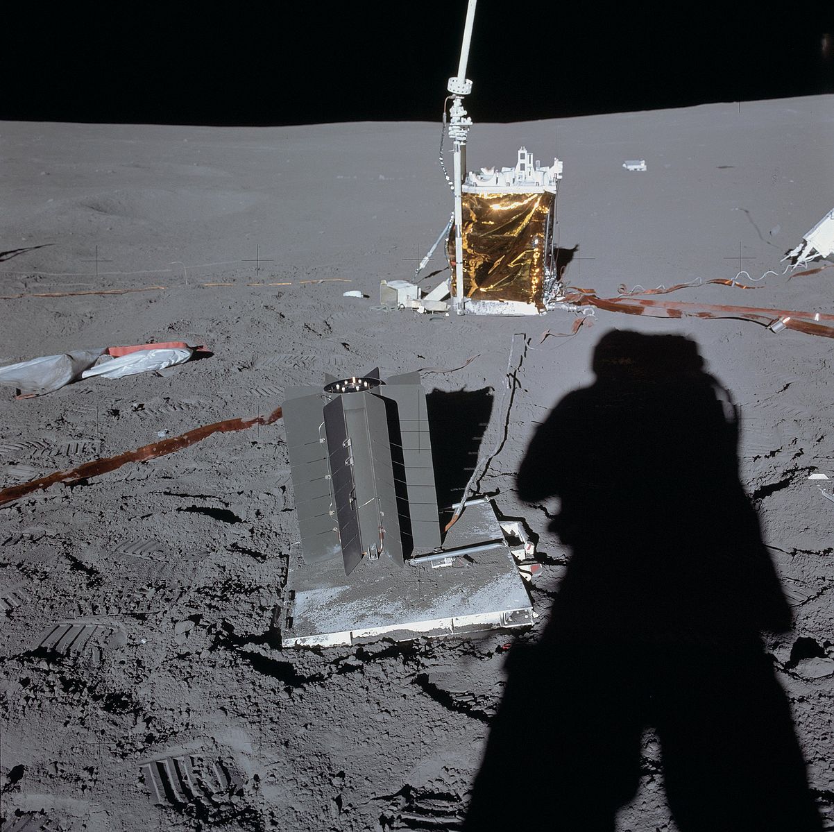 An astronaut casts a long shadow on the Moon as he photographs scientific equipment on the lunar surface.