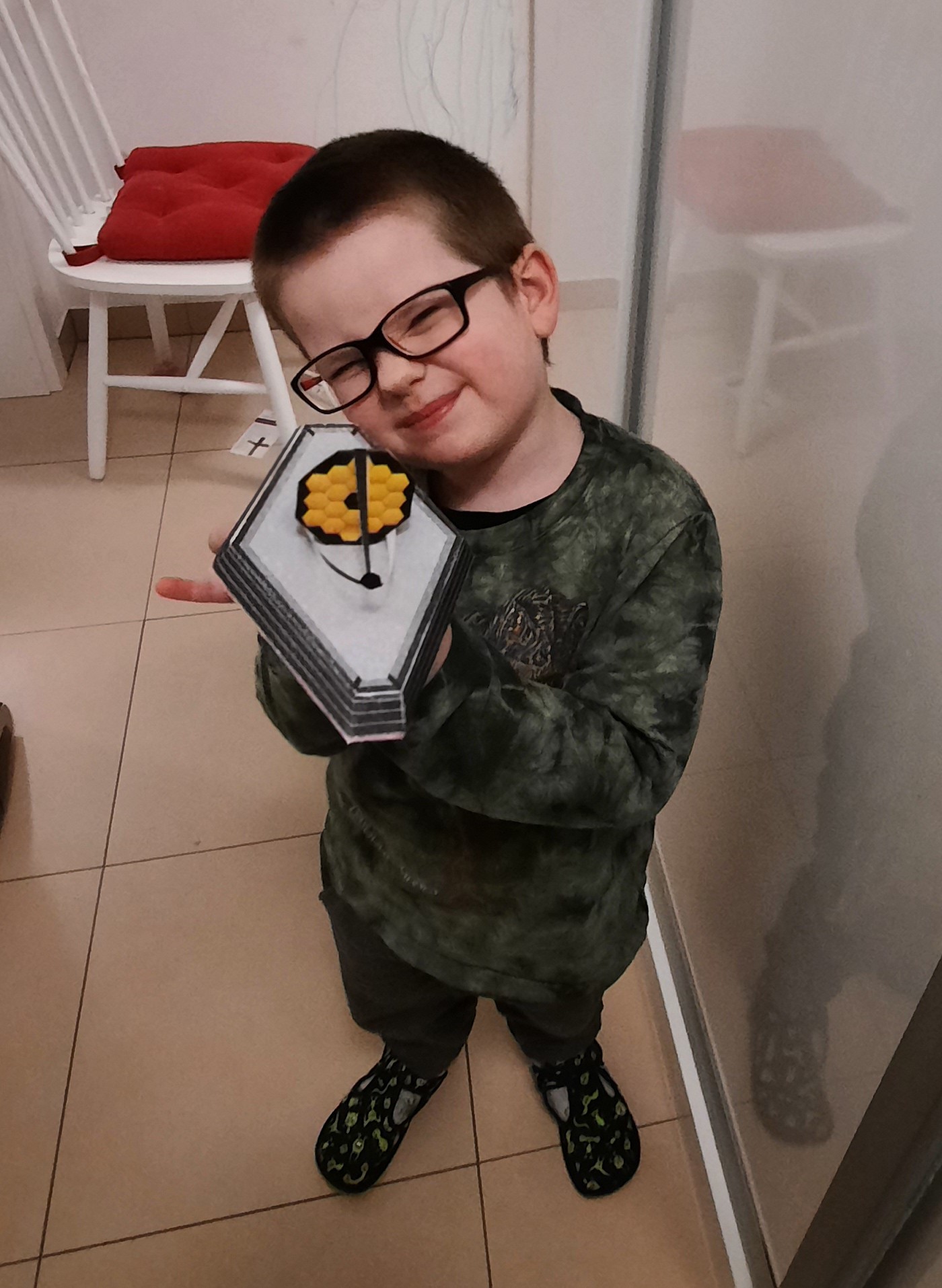 a four year old young boy holds a model oif JWST he built