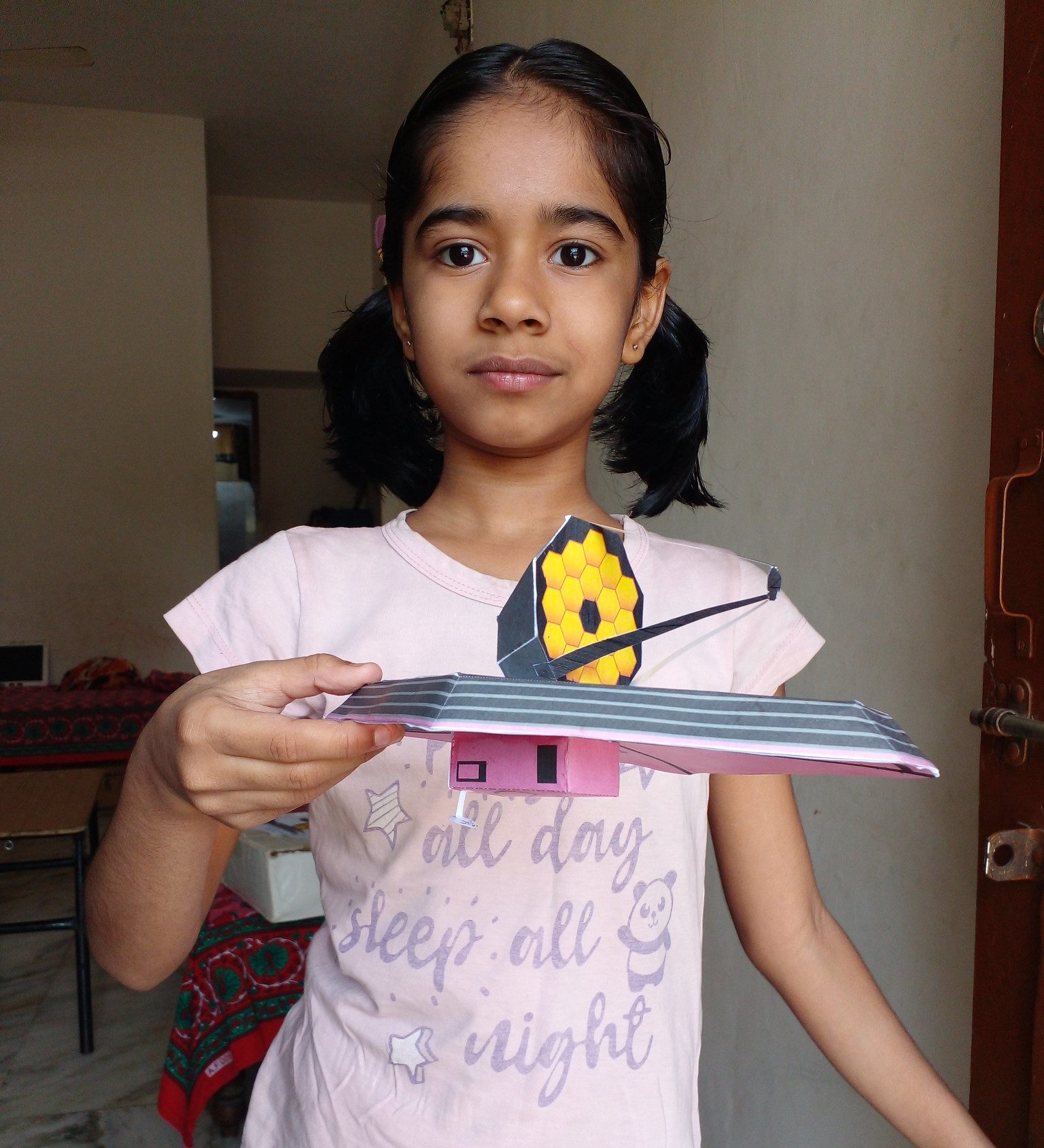 a young girl holding a model of JWST she built