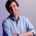 brown-haired man in blue dress shirt with his arms folded, smiling