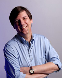 brown-haired man in blue dress shirt with his arms folded, smiling