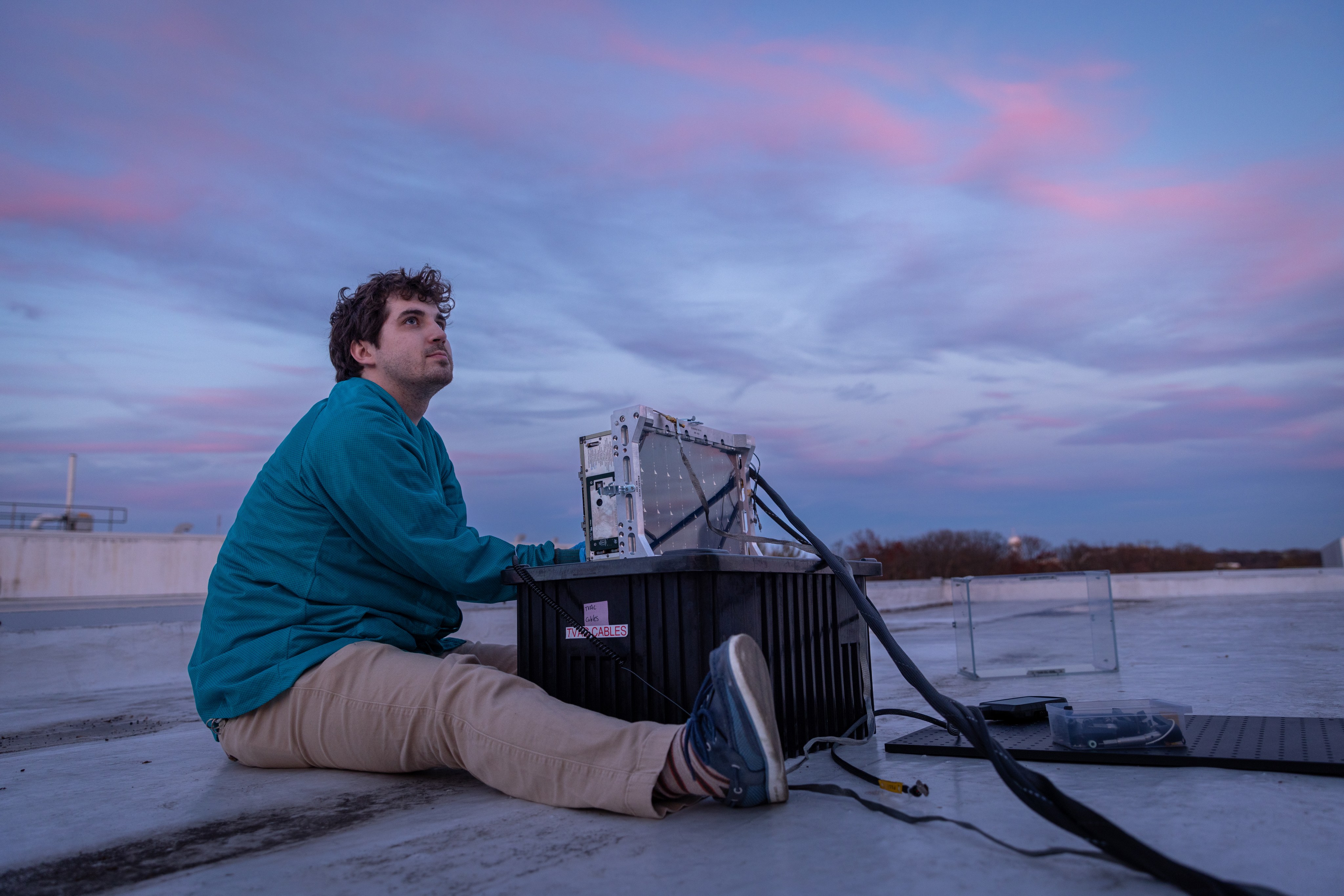 This photograph shows a man sitting next to a spacecraft on a rooftop.