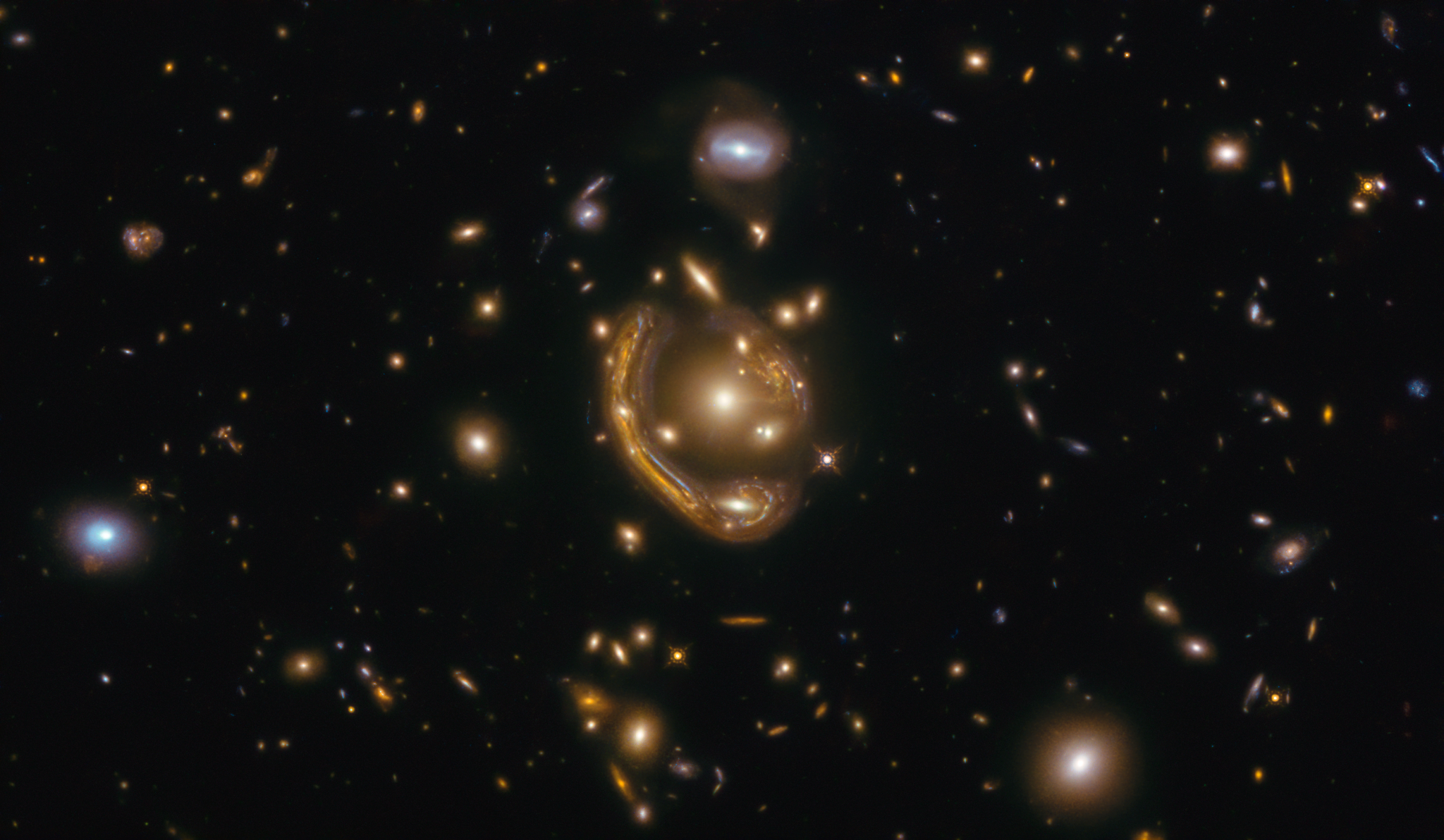 A black background dotted with galaxies. Image center holds a cluster of galaxies with a distinct arc nearly surrounding it.