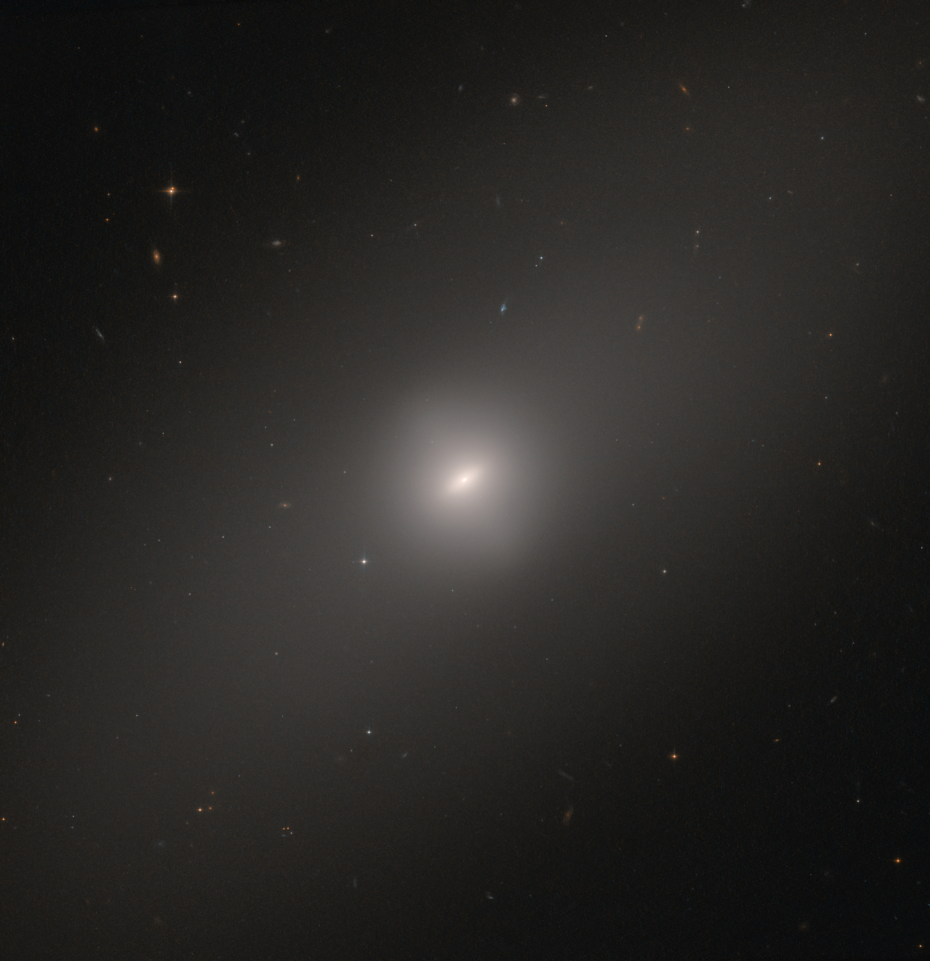 A black background dotted with galaxies. A bright galaxy is at image center. It looks like a diffuse ellipse that stretches from the lower-left corner to the upper-right corner, with a bright core at image center.