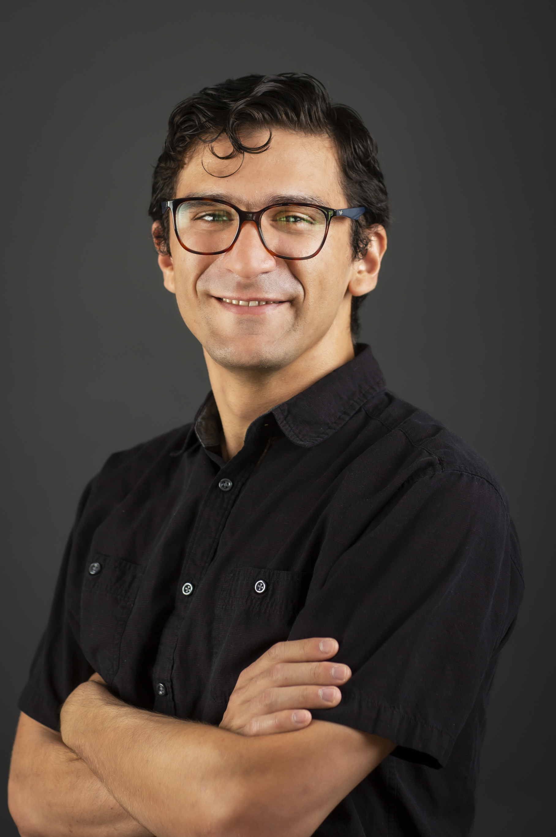 wavy dark-haired man with glasses in black short-sleeved dress shirt in formal headshot