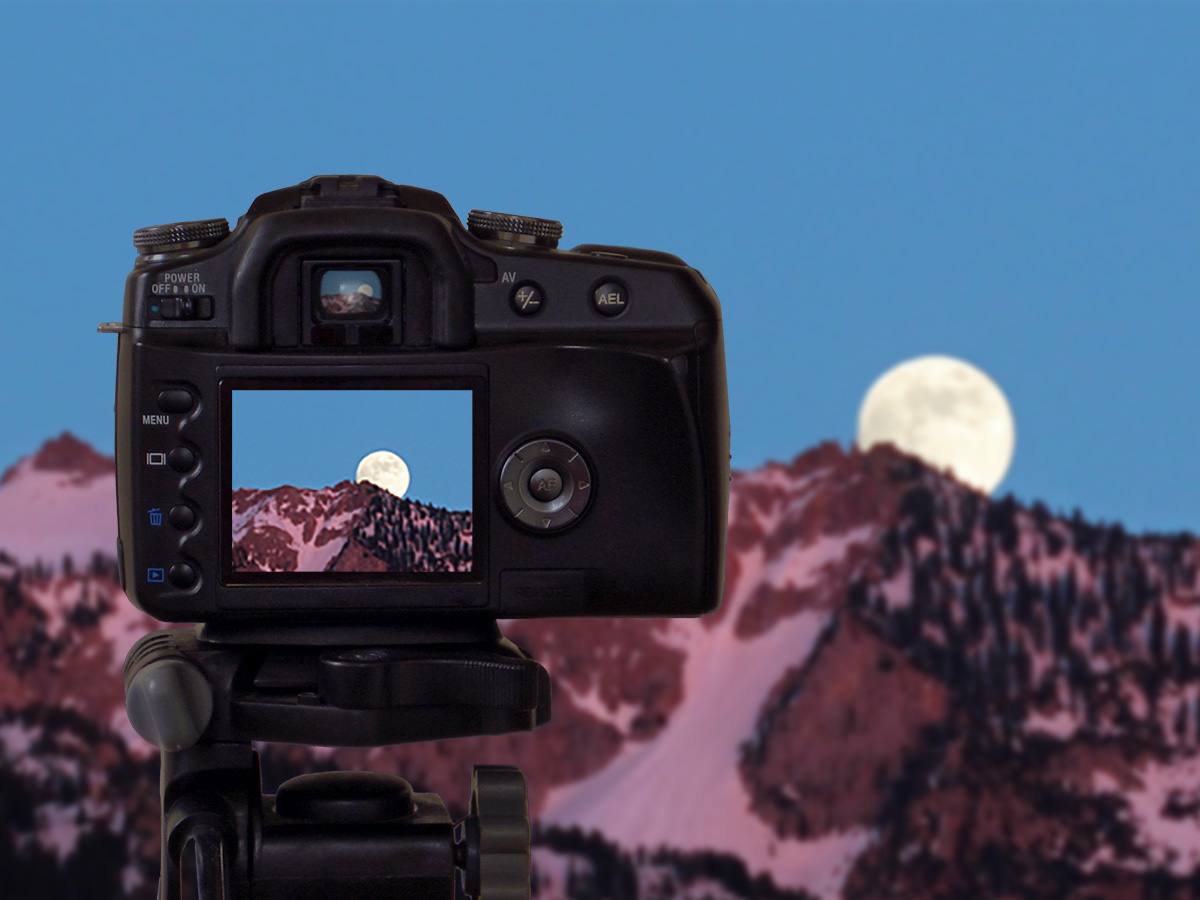 Composite photo image of a camera in front of a mountain landscape with the Moon over the horizon