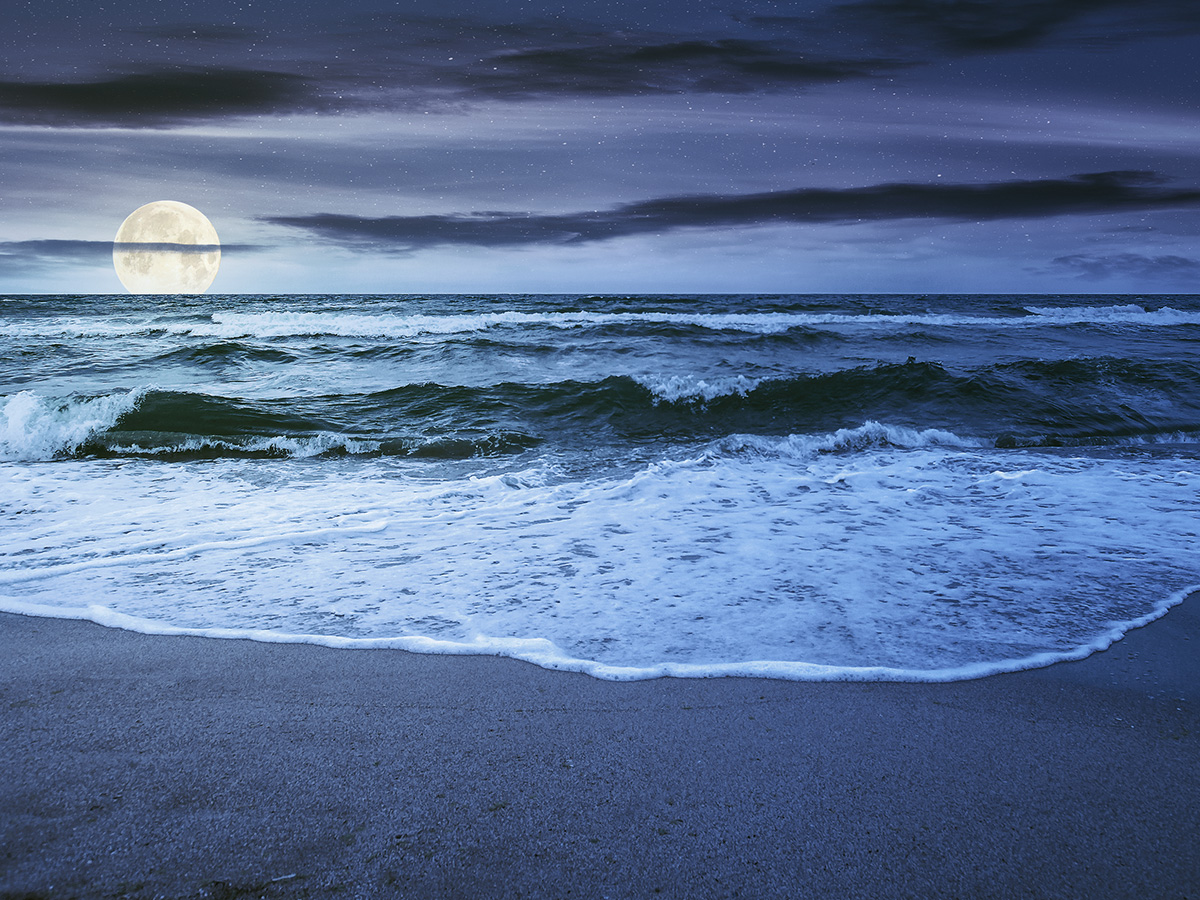Photo of ocean tides coming in on beach, with Moon behind horizon.