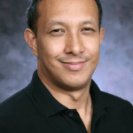 headshot of man with short, dark hair in black collared shirt