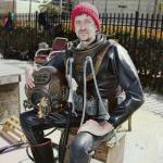 seated, goateed man in red knit cap holding diving helmet and wearing full diving gear