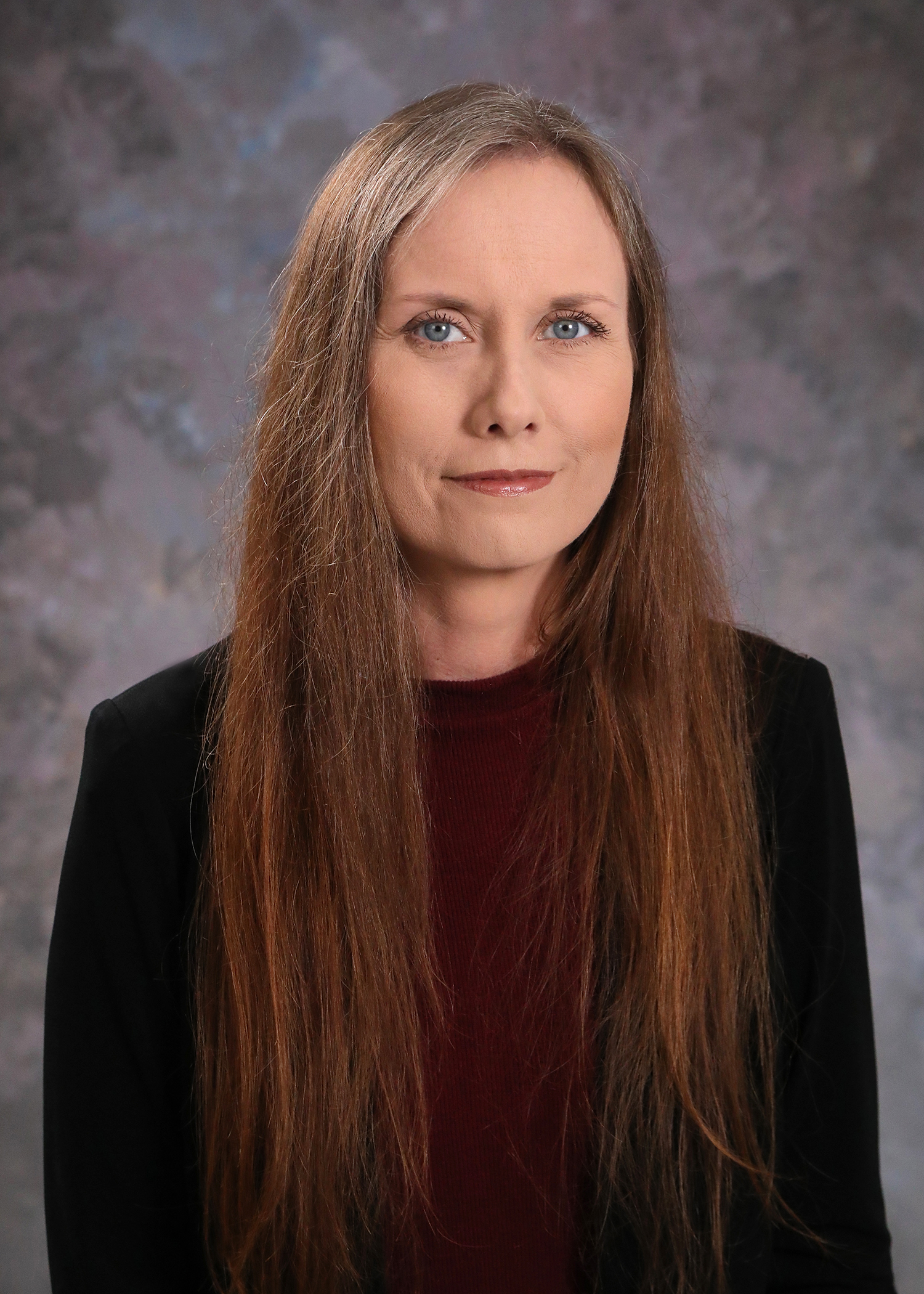 headshot of woman with long amber-colored hair wearing black blazer and burgundy crew neck top