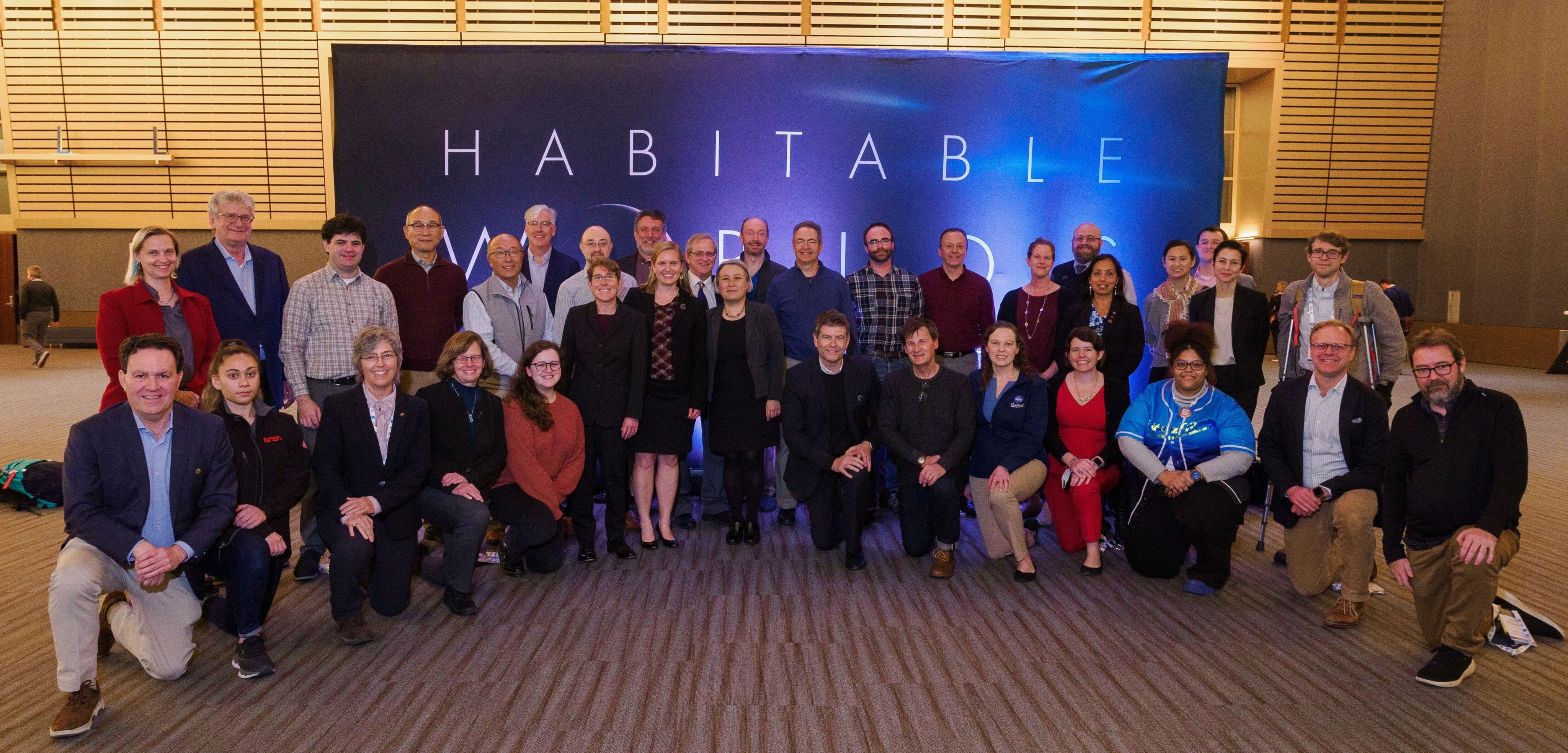 A photo of the START and TAG teams and other staff at the 2024 winter AAS meeting. The team is posing in two rows and standing in front of a sign that says "Habitable Worlds Observatory."