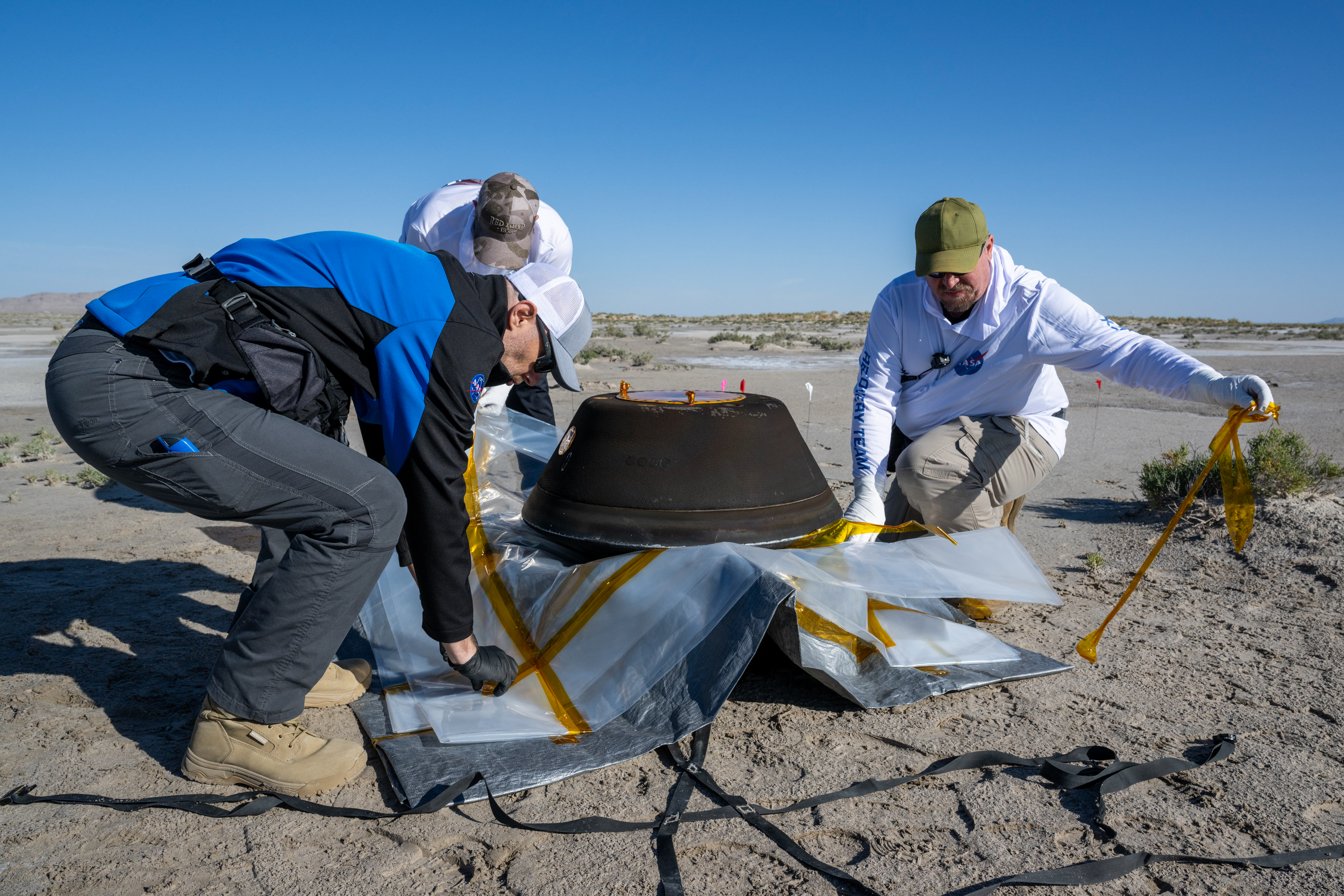 Three men prepare the sample for transport by helicopter in the desert.⁣