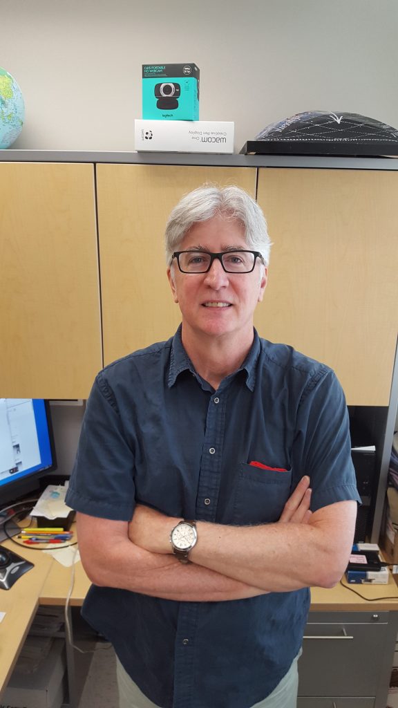 Portrait photo of a man standing in an office with his arms crossed.