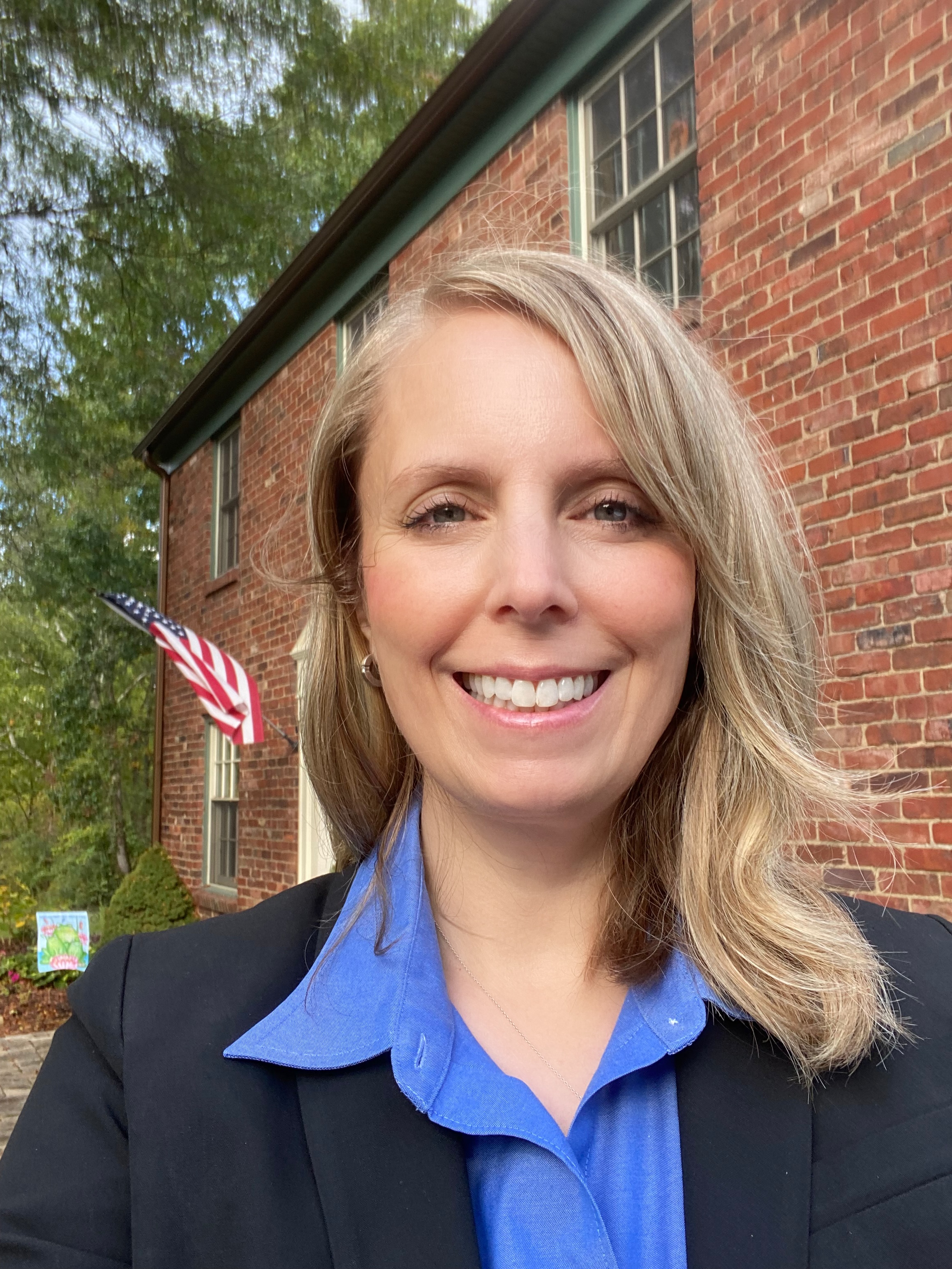 Erica N. Montbach outside a brick building with blonde hair, a blue collared shirt, and a dark jacket.