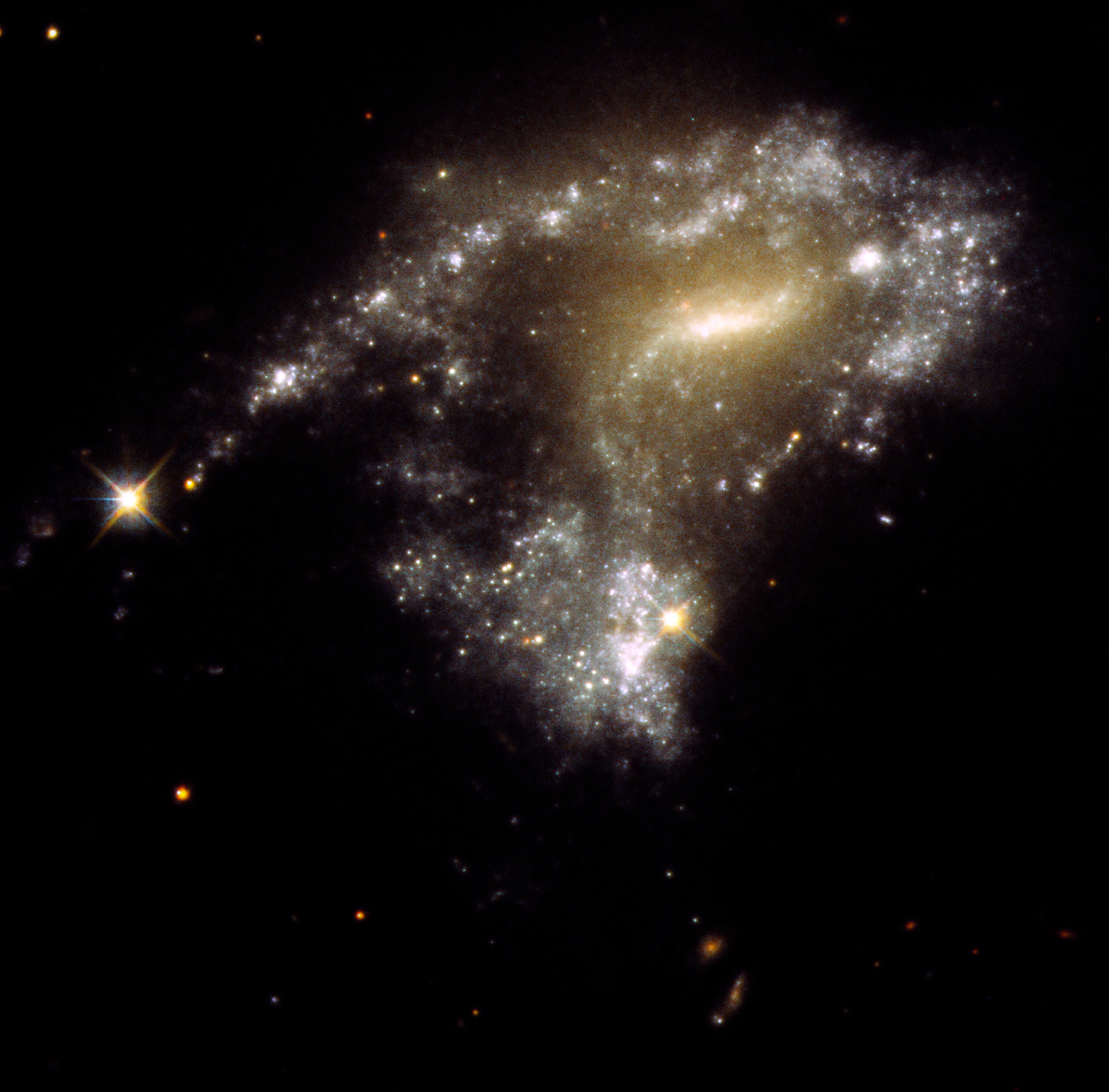 This is a picture of a galaxy with a peculiar S-shape. It has a bright milky-white core at the center. Twin arms of blue stars wrap around the core. One arm looks particularly stretched out due to the gravitational tidal pull of a neighboring galaxy. Bright, young, whitish star clusters are strung along the arm like a string of pearls. They formed as a result of the collision process.
